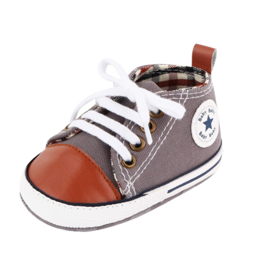 Detaljerad babysneaker i grå / brun färg. Bild tagen snett framifrån. Bebisskor, babyskor